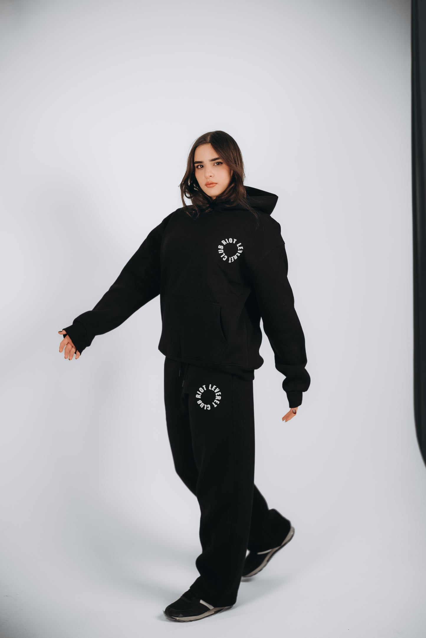 A Unisex Black set in a Relaxed Fit. The Model is wearing the Riot Leveret Club, a Unisex Black crafted from premium Egyptian cotton with a soft-touch finish. It features white rubber print details, an elastic waistband, and ribbed cuffs for a sleek and comfortable look.