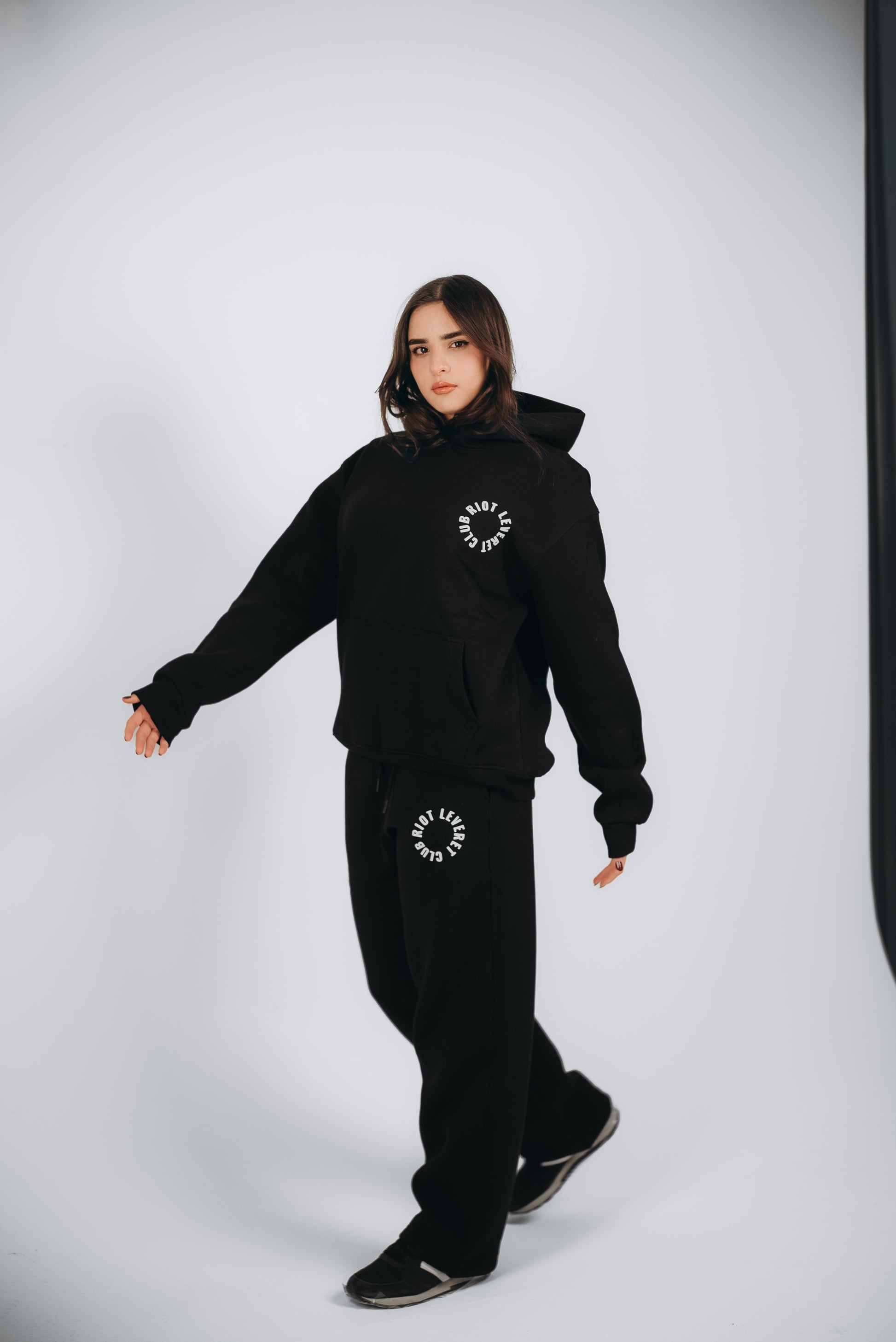 A Unisex Black set in a Relaxed Fit. The Model is wearing the Riot Leveret Club, a Unisex Black crafted from premium Egyptian cotton with a soft-touch finish. It features white rubber print details, an elastic waistband, and ribbed cuffs for a sleek and comfortable look.