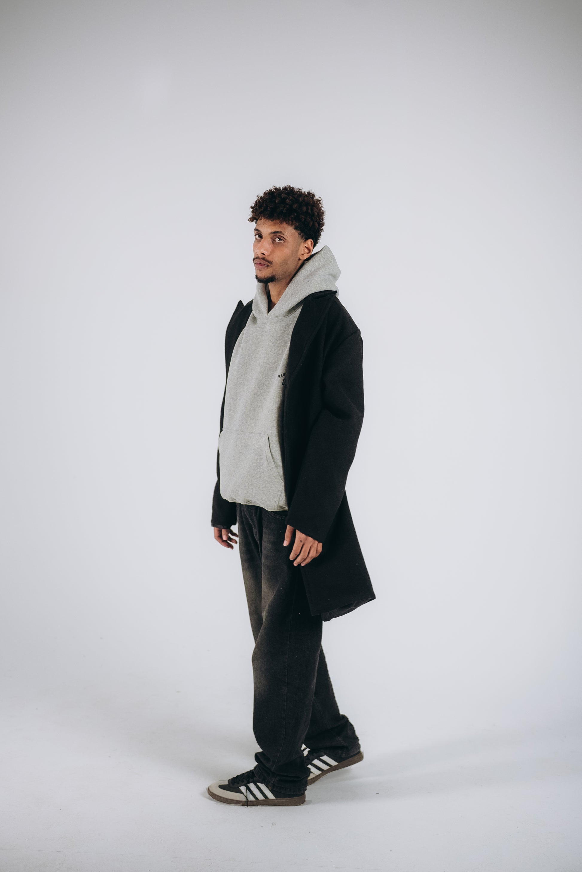 the young man wears gray hoodie, jeans pants, and black wool blended coat