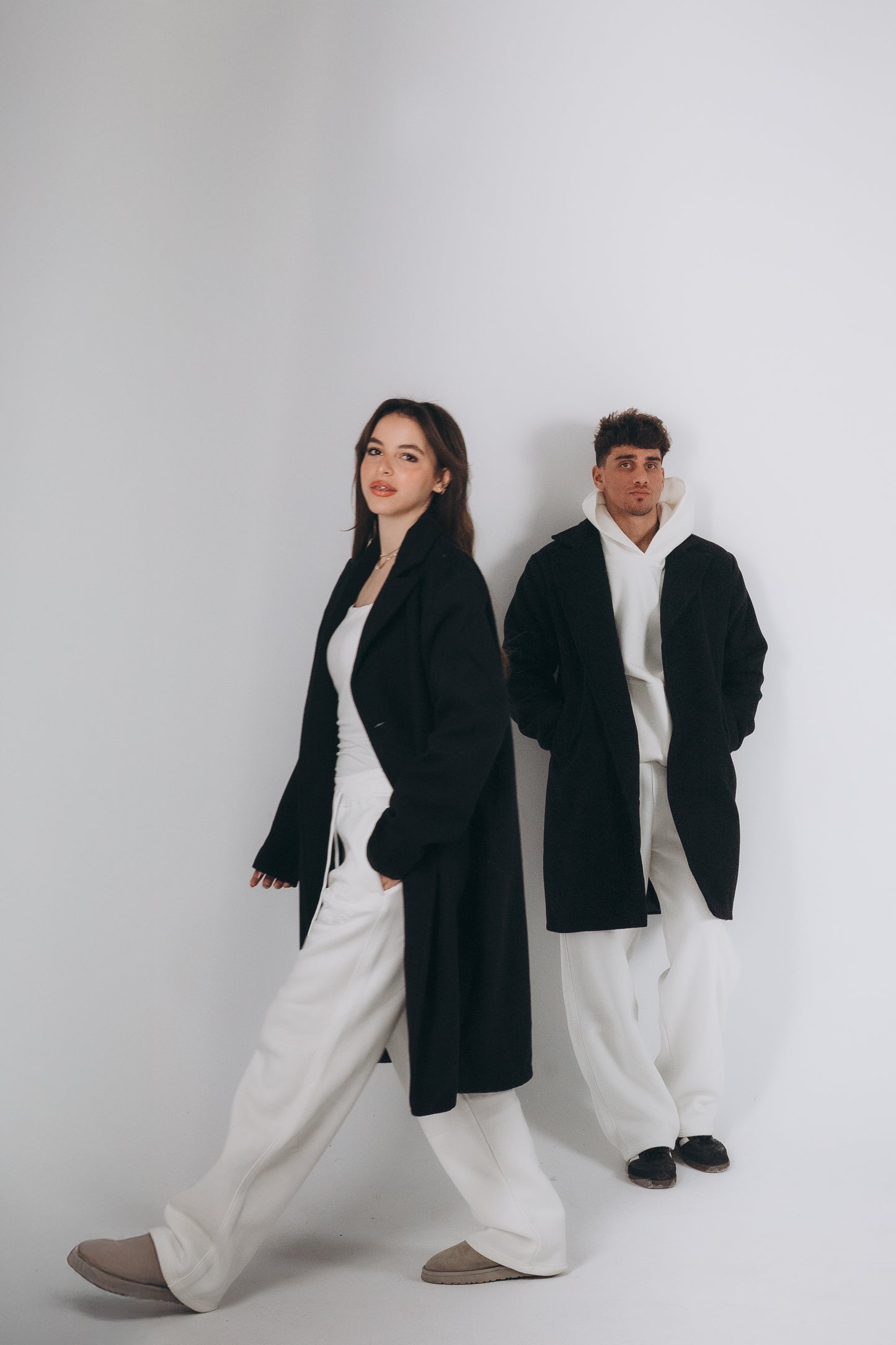 Two models are wearing oversized black coat layering with white set of hoodies and sweatpants